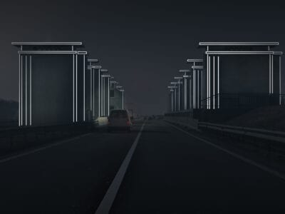 Gates of Lights in het donker met lichtstrips. Door reflectie van de koplampen lichten de strips links en rechts op. Links rijdt een witte bestelbus.