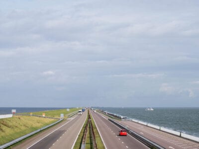 Foto van de Afsluitdijk. Je ziet de snelweg met twee keer twee rijbanen. Eén heen en één terug. Aan beide kanten zie je het water van het IJsselmeer en het water van de Waddenzee.