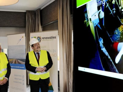 Presentatie over de proefinstallatie op stromingsenergie. Gedeputeerde Bond en Gedeputeerde Konst kijken samen naar een scherm waarop de motoren van de stromingsenergie te zien zijn.