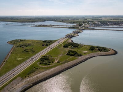 Luchtfoto van Den Oever, de Stevinsluizen. We kijken van boven op de dijk. Je ziet linksonder een weg lopen naar Den Oever. Links is om de weg een landstrook.