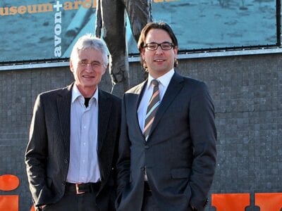 Portretfoto van Jan en Joost. Deze twee mannen staan naast elkaar voor een donker gebouw.