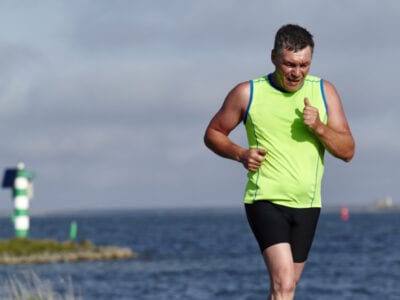 Hardloper bij de Afsluitdijk Open. Hij heeft een groen shirt aan en op de achtergrond zie je water.