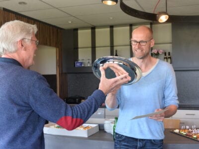 Overhandiging van de Biermanprijs (een zilveren schotel). De overhandiging is van de ene man aan de ander. De foto is van achter genomen en op de foto staat een klein stukje van een derde man.