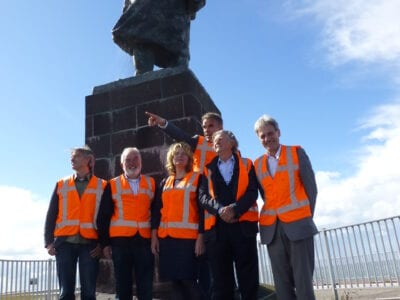 Kwaliteitsteam bij het standbeeld van Lely. We zien zes mensen in pak en oranje hesjes. Zij staan voor het standbeeld.