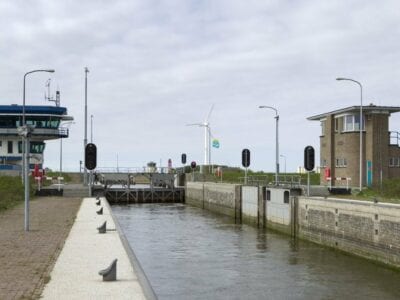 De Schutsluis bij Den Oever. Met het wit en blauwe sluisgebouw en een windmolen op de achtergrond.