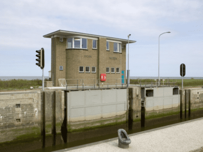 Stevinsluizen. Wij kijken uit over het water bij de sluis. Aan de kade staat een groot, geblokt sluisgebouw.