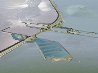 Impressie van de Vismigratierivier. Je ziet een getekende versie van de Afsluitdijk. In de Afsluitdijk is de Vismigratierivier getekend. Dit is een slingerende rivier, omlijnd met grondstroken. Aan de kant van de Waddenzee zie je een uitmondingshaven.