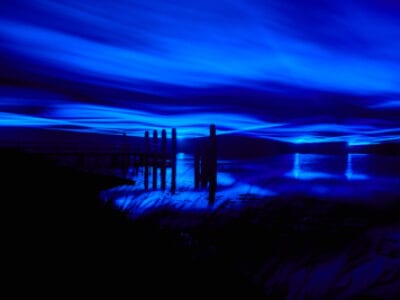 Wij kijken uit over de Afsluitdijk. De foto is erg donker maar je ziet dat de lucht blauw gekleurd is met strepen.