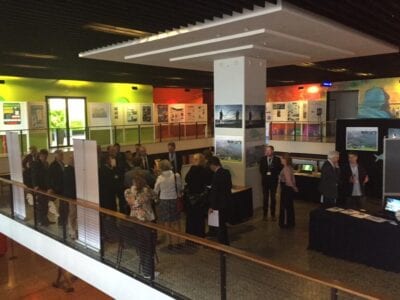 Een conference over de vispassage. Er staan meerdere mensen in de expositiehal. Aan de gekleurde wanden zie je afbeeldingen van de vispassage en de Blije Vis.