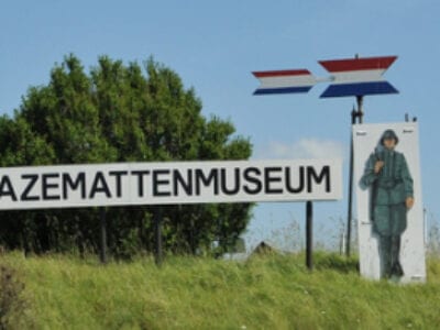 Afbeelding van een duin met een bord erop: Kazemattenmuseum. Rechts staat er ook een getekende soldaat.