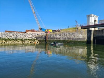 Wij zien het water van de Afsluitdijk. Aan de achterkant zie je een stuk dijk. In het water, voor de dijk, ligt een detectieboot. Links zien we een steiger.