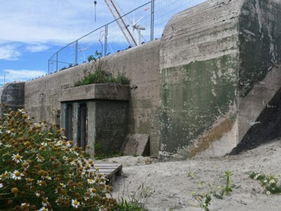 Op de foto zie je een grijsgroene bunker. In het midden van de bunker zit de ingang zit de deur.