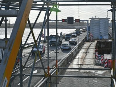 Werkzaamheden bij Stevinsluizen, je ziet een weg met een hekwerk ervoor. Op de weg rijden meerdere auto's 50 km per uur. Dit weet je omdat het op het bord boven de weg staat.