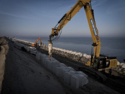 De dijk wordt versterkt door middel van het plaatsen van blocs door een kraan.