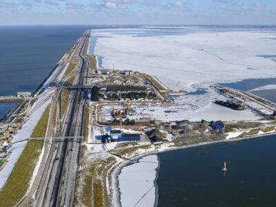 Een winterfoto uit de lucht van de Blue Energy Centrale. We zien de Afsluitdijk met water aan weerskanten.