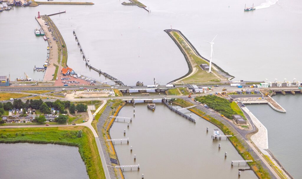 Luchtfoto op water met erin draaubruggen, een weg en strekdammen.