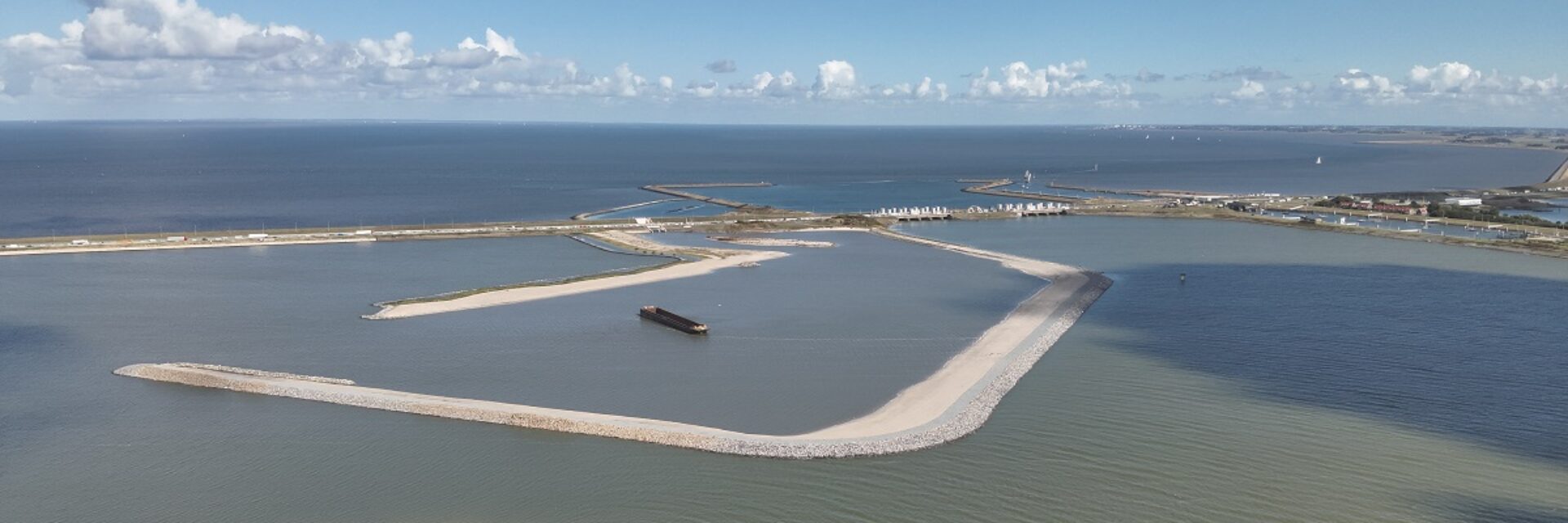Luchtfoto met zicht op water waarin een aantal dammen te zien zijn. Bovenin de lucht met kleine witte wolkjes,