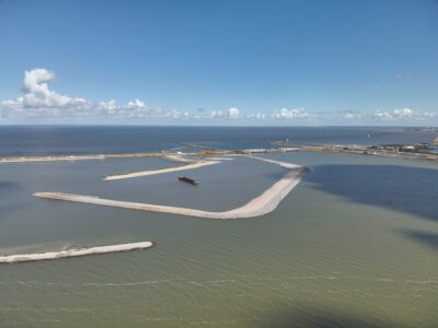 Luchtfoto met zicht op water waarin een aantal dammen te zien zijn. Bovenin de lucht met kleine witte wolkjes,