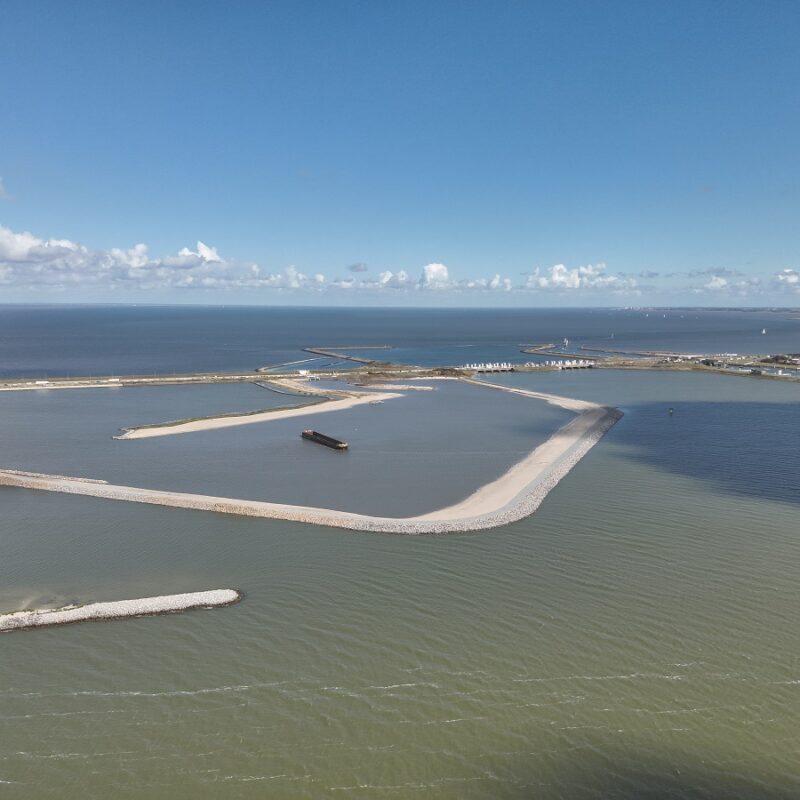 Luchtfoto met zicht op water waarin een aantal dammen te zien zijn. Bovenin de lucht met kleine witte wolkjes,