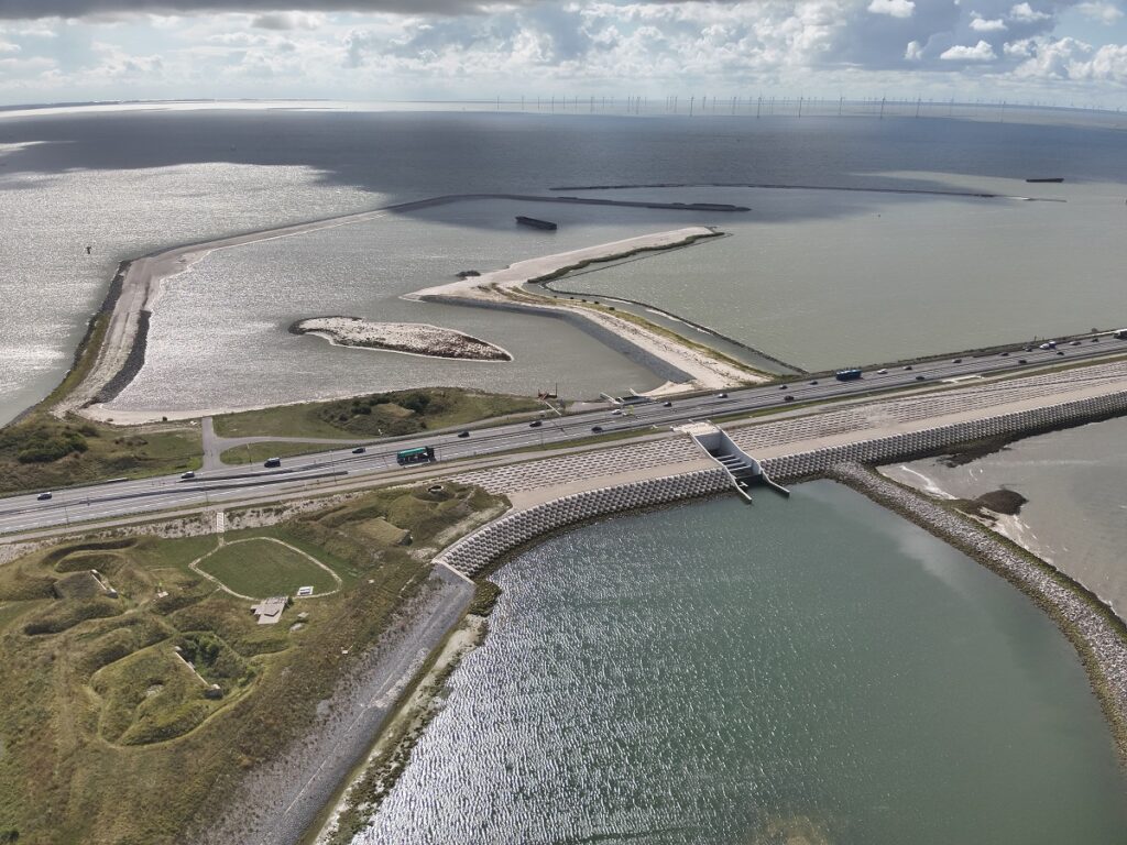 Luchtfoto zicht op de Afsluitdijk met de doorgang door de dijk. Erboven en onder zijn dammen in het water te zien.