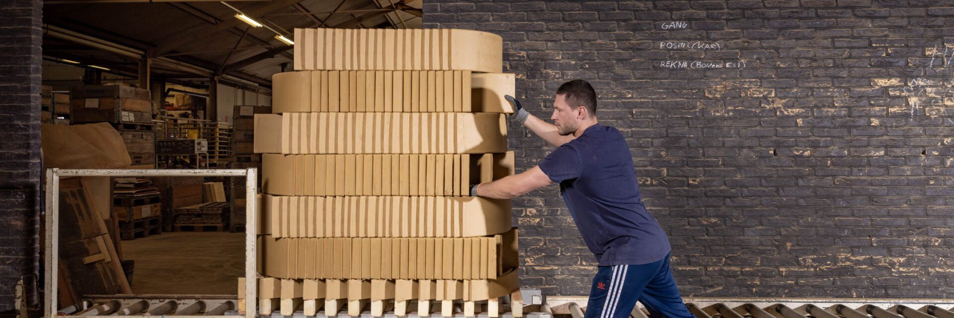 Een kar met stapels lichtgele tegels wordt in een loods weggereden door een medewerker.