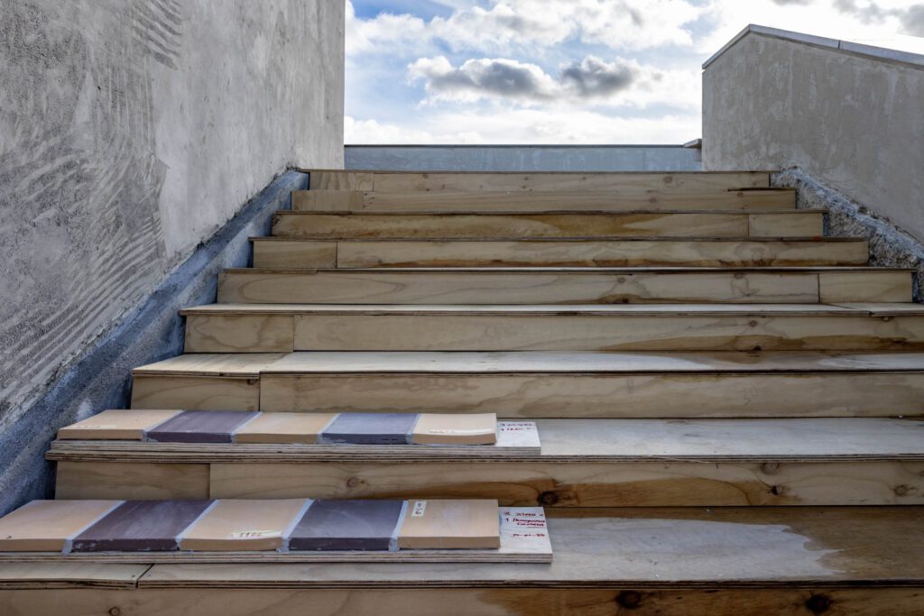 Een brede trap, gezien van onderaan. Op de onderste twee tredes liggen om en om enkele lichtgele en donkerpaarse tegels. 