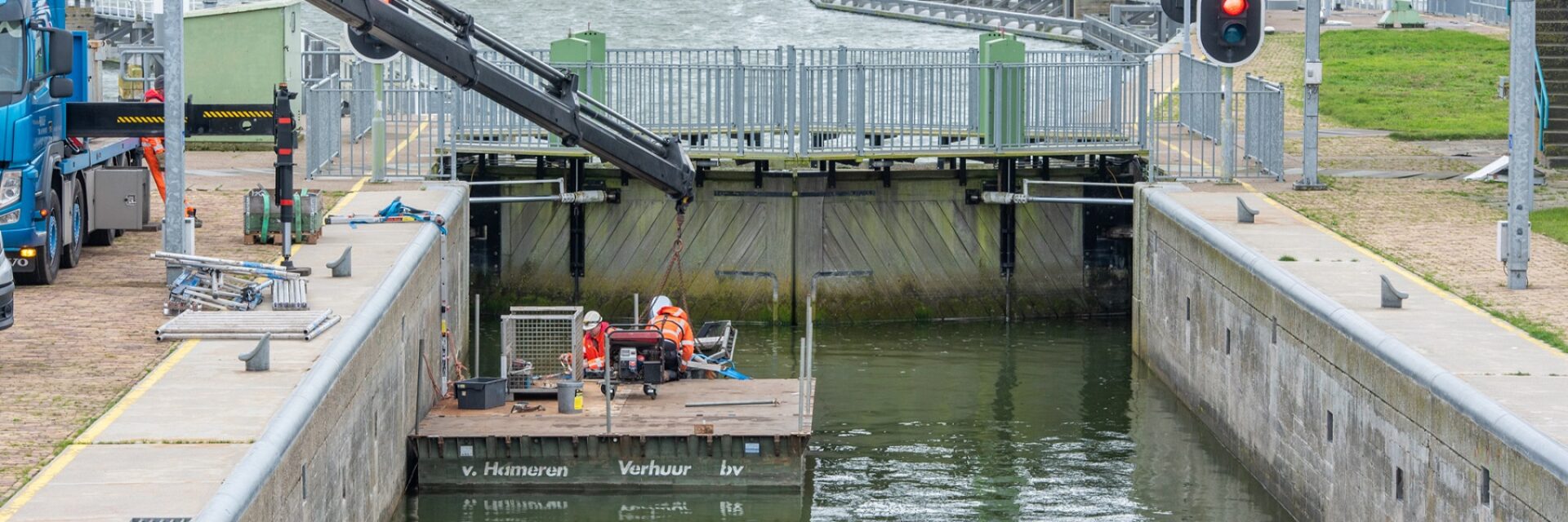 We zien de binnenkant van een sluis met een vlot met een aantal medewerkers die aan het werk zijn.