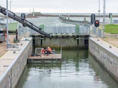 We zien de binnenkant van een sluis met een vlot met een aantal medewerkers die aan het werk zijn.