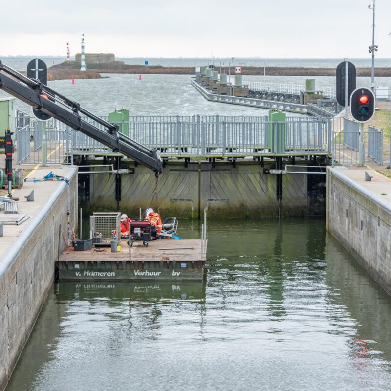 We zien de binnenkant van een sluis met een vlot met een aantal medewerkers die aan het werk zijn.