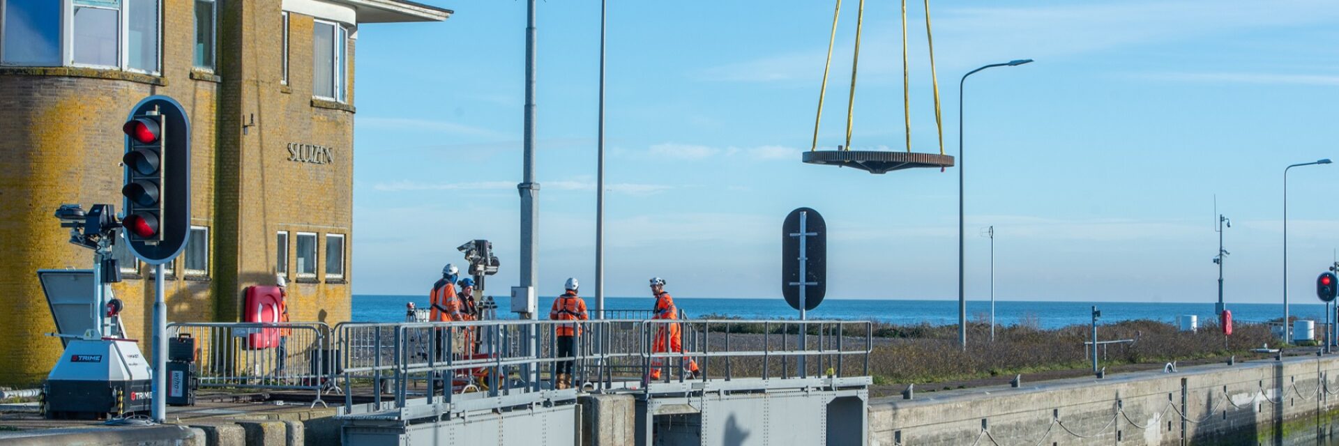 We zien dat een tandwiel in de lucht gehesen is bij een sluiscomplex.