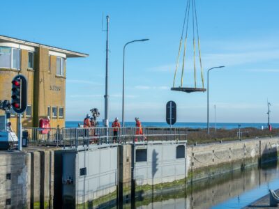 We zien dat een tandwiel in de lucht gehesen is bij een sluiscomplex.