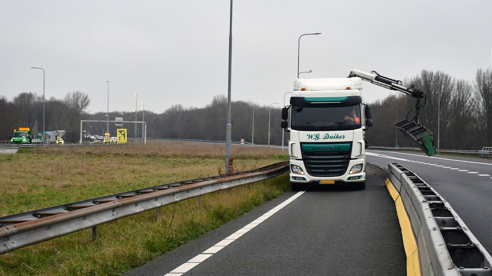 We zien dat een grijper op een vrachtwagen de tijdelijke vangrails verwijdert.