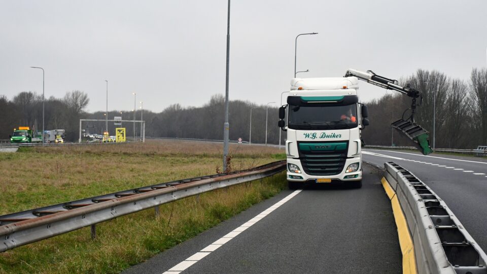 We zien dat een grijper op een vrachtwagen de tijdelijke vangrails verwijdert.