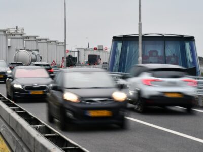 we zien auto's rijden over de rijbaan met op de achtergrond witte gebouwtjes en een koepel die typerend zijn voor de Afsluitdijk.