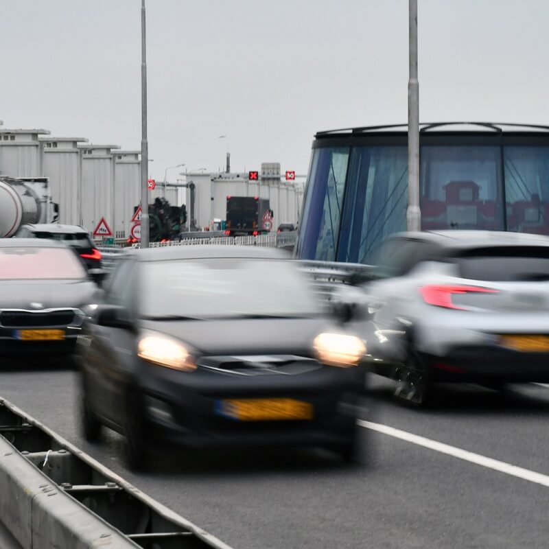 we zien auto's rijden over de rijbaan met op de achtergrond witte gebouwtjes en een koepel die typerend zijn voor de Afsluitdijk.
