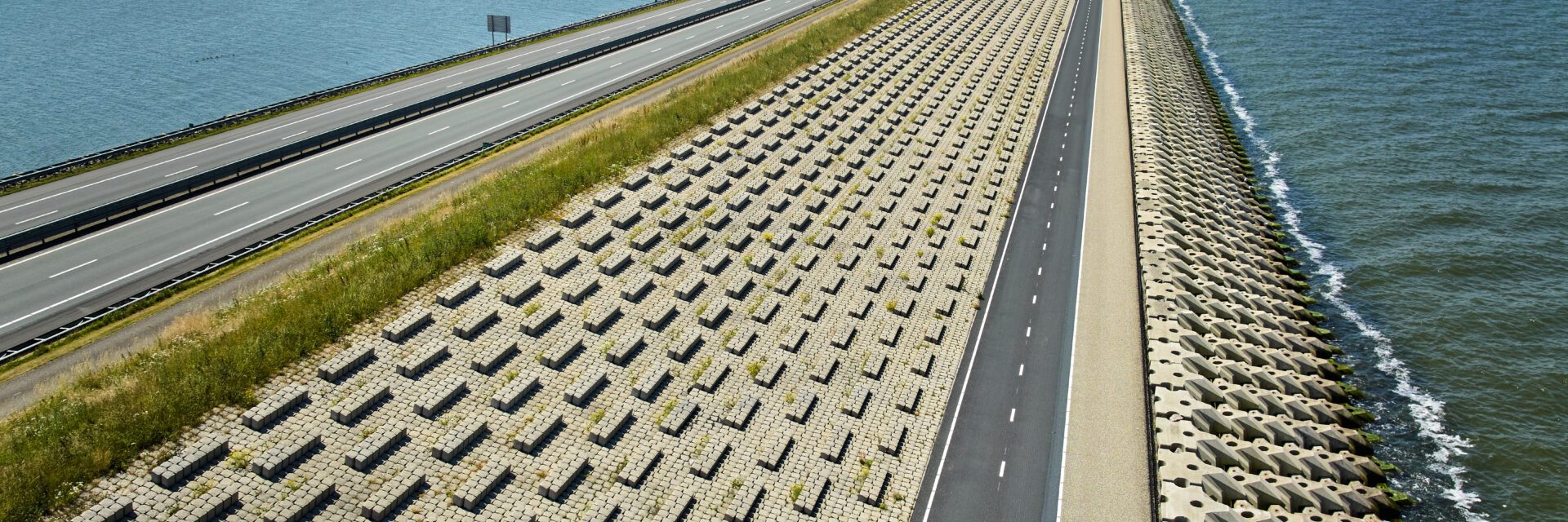 Een panoramazicht van de Afsluitdijk, de snelweg A7 en het nieuwe fietspad, met aan de linkerzijde het IJsselmeer en de rechterzijde de Waddenzee.