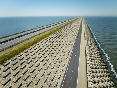 Een panoramazicht van de Afsluitdijk, de snelweg A7 en het nieuwe fietspad, met aan de linkerzijde het IJsselmeer en de rechterzijde de Waddenzee.