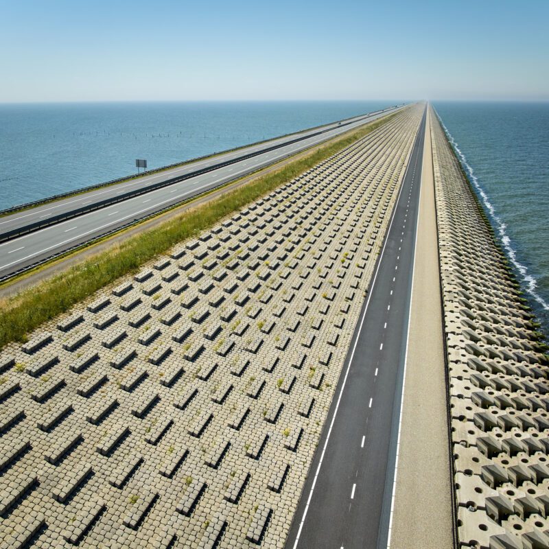 Een panoramazicht van de Afsluitdijk, de snelweg A7 en het nieuwe fietspad, met aan de linkerzijde het IJsselmeer en de rechterzijde de Waddenzee.