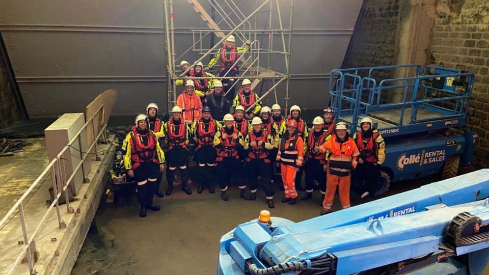 Een groep mensen staan geposeerd voor een foto. De mensen hebben allen reddingsvesten aan.